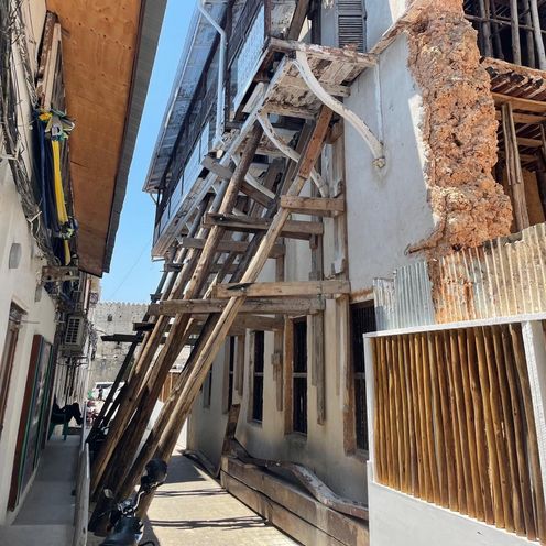 2026 Projekt Sassibar CO3 Bild zeigt schmale Gasse. Die Hausfassaden sind sanierungsbedürftig. Die rechte stützt ein Holzgerüst.