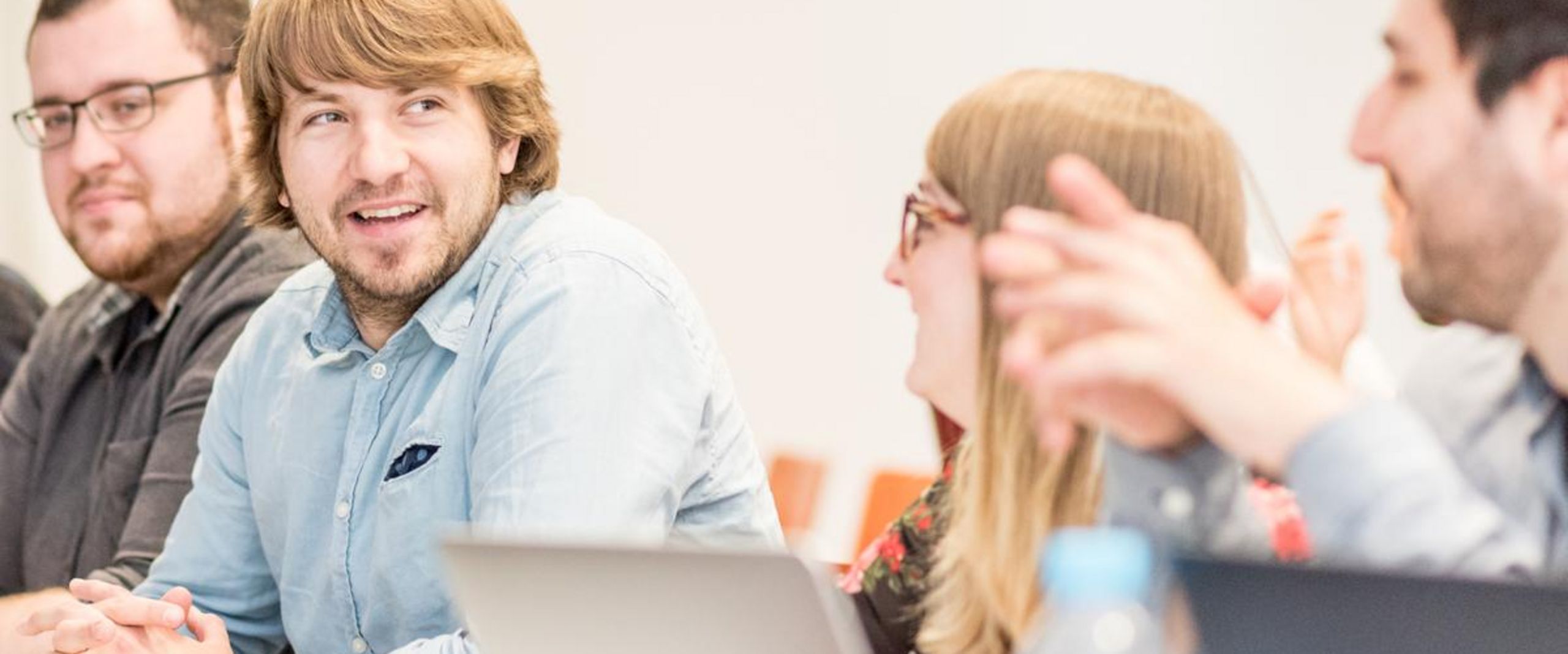 Austausch und Teamarbeit im Seminar Vier Studierende sitzen gemeinsam an einem Tisch, unterhalten sich und arbeiten mit Laptops. Die Stimmung wirkt konzentriert und freundlich.