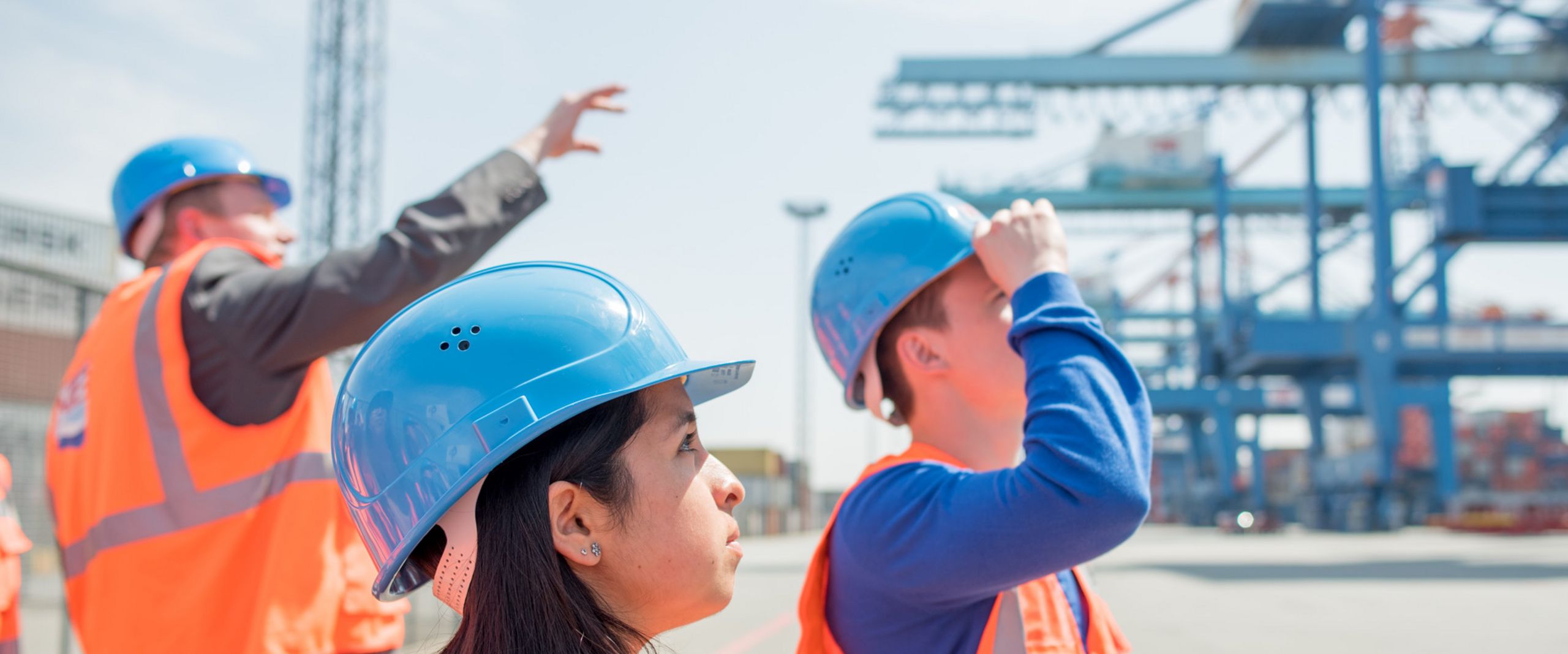 Exkursion zum Containerterminal Ein Beschäftigter führt Studierende in Warnwesten und Schutzhelmen durch ein Containerterminal.