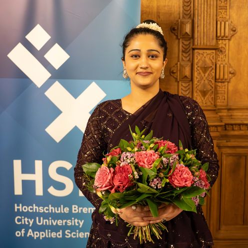 DAAD-Preisträgerin 2025 Sannae Kapoor Frau Mit Blumen vor einem Roll-up