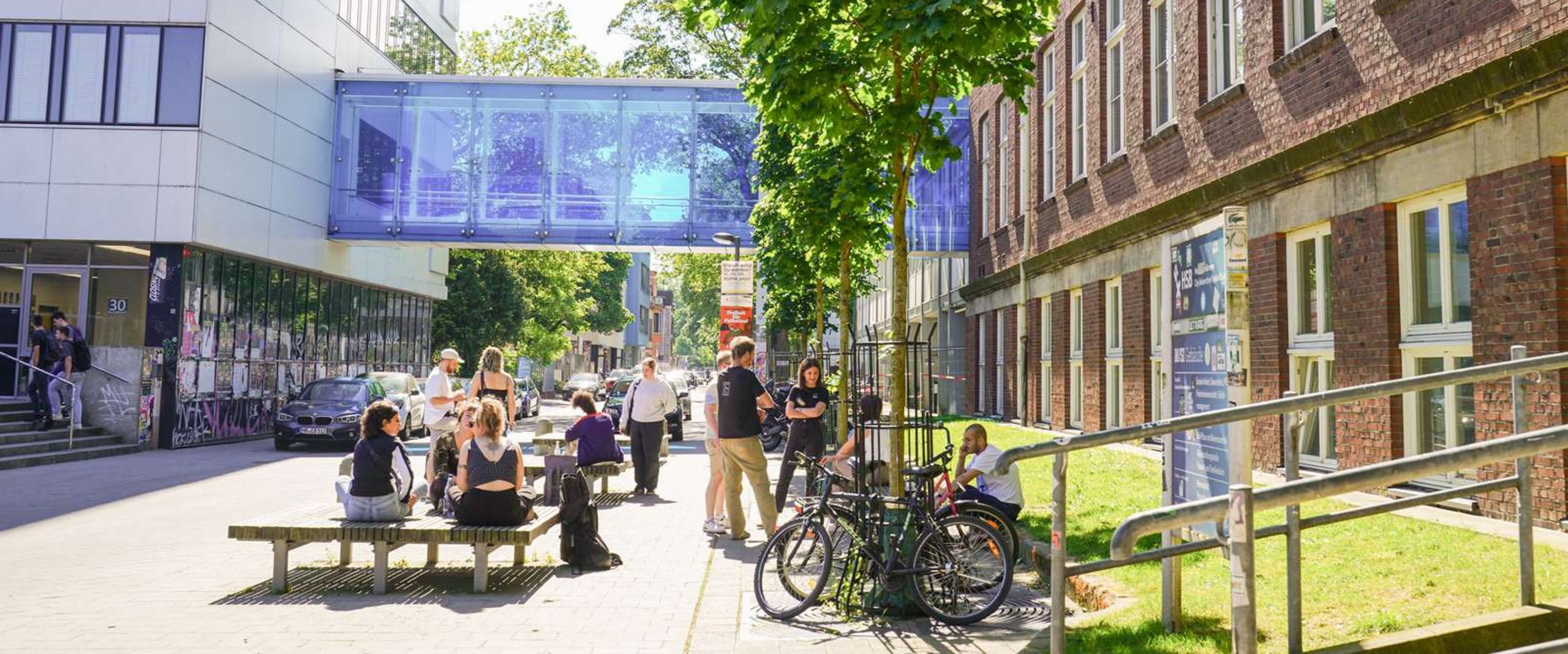 Campus am Neustadtswall Studierende auf den Sitzgelegenheiten am Campus Neustadtswall bei sonnigem Wetter. Im Hintergrund sind das AB-Gebäude mit einer blauen verglasten Brücke sowie das M-Gebäude zu sehen.
