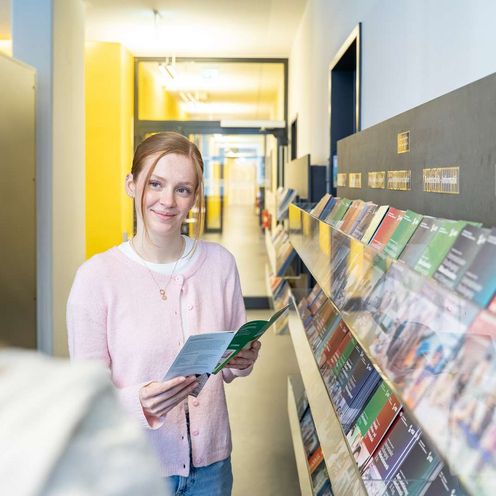 Studienwahl Auf dem Bild ist eine junge Frau zusehen. Sie hält einen Flyer in der Hand und schaut knapp an der Kamera vorbei.