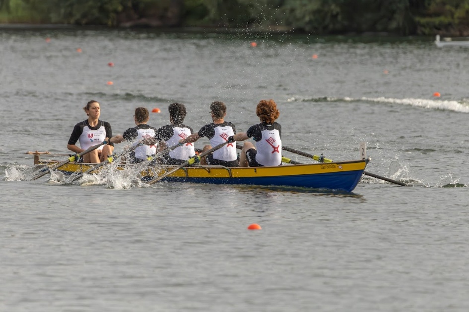 DHM Rudern_2025_Männervierer Vier Ruderer sitzen gemeinsam während der Deutschen Hochschulmeisterschaft Rudern in einem Boot. Vor ihnen sitzt eine Steuerfrau