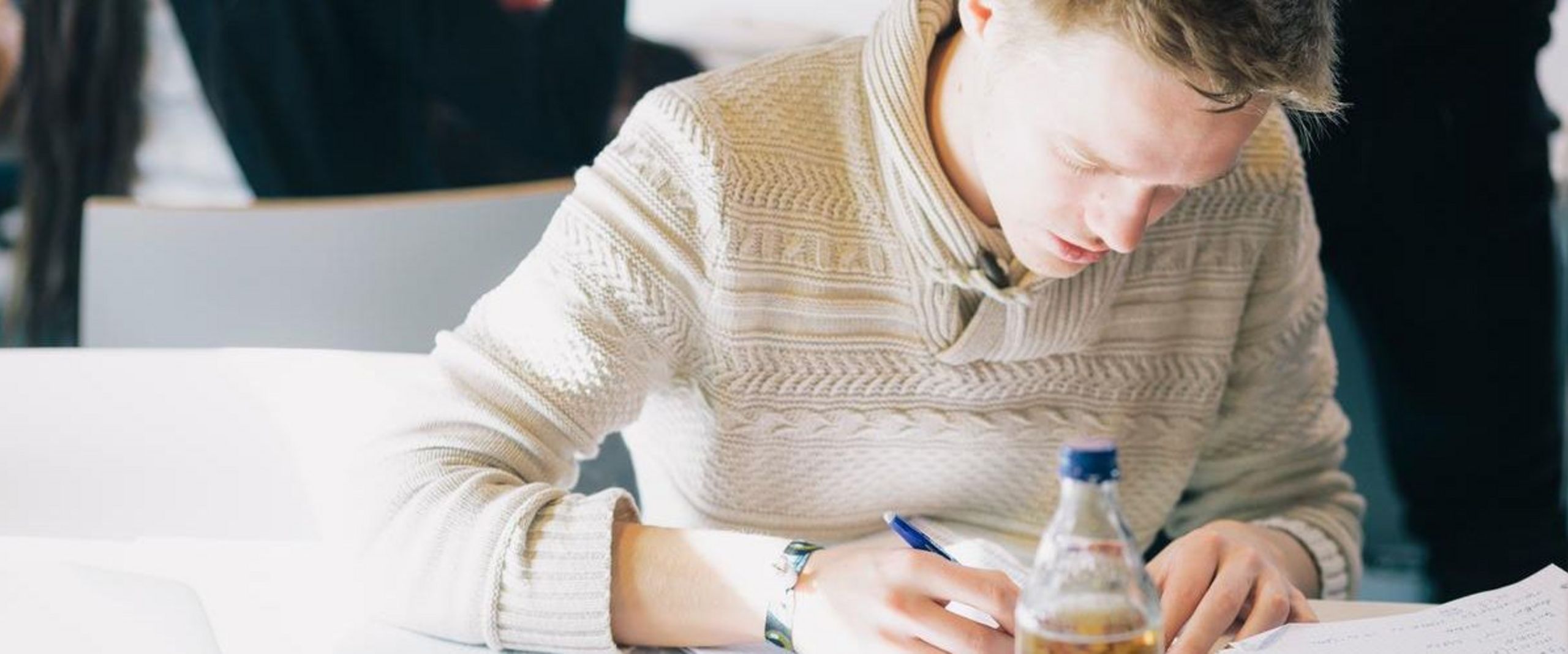 Student beugt sich über Schreibtisch und schreibt etwas auf Papier. 