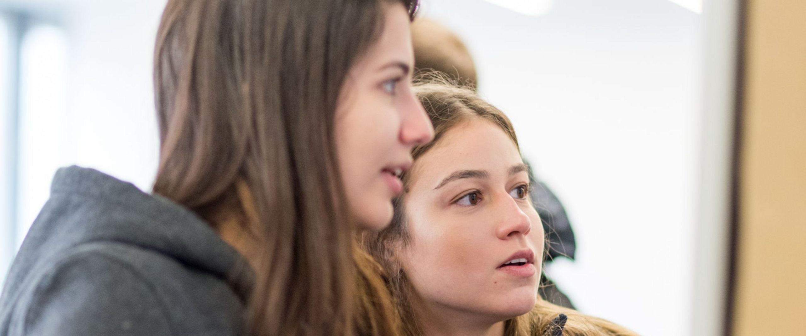 Zwei junge Studentinnen betrachten interessiert eine Pinnwand 