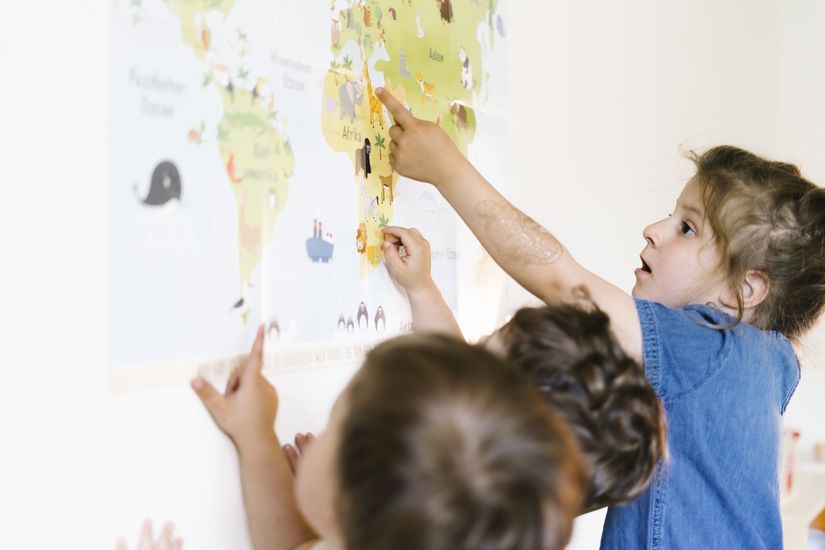 Kinder mit Weltkarte Kinder zeigen auf eine große Weltkarte