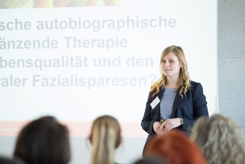 Lebensqualität, Therapie und Gesundheit Auf dem Bild ist eine junge Frau zusehen, die eine Präsentation vor einem Publikum hält.