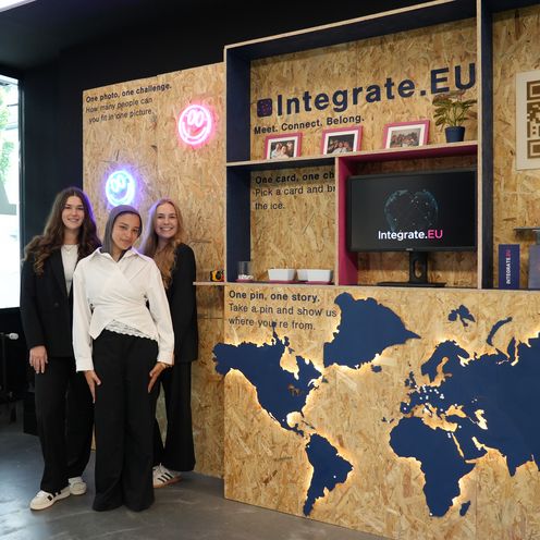 STARS EU Projekt Integrate.eu Drei junge Frauen stehen vor einer Präsentation mit Landkarte und Regalfächern