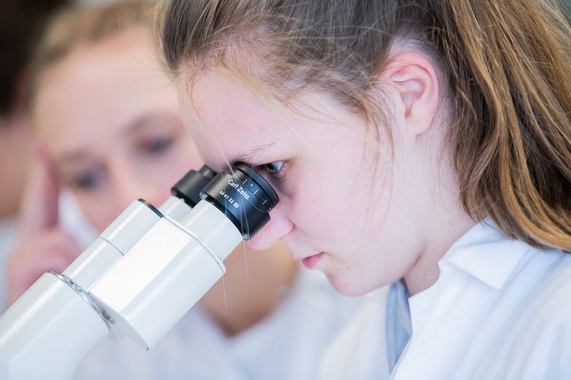 Laborübung in der Bionik Eine Studentin in Laborkittel blickt in ein Mikroskop.