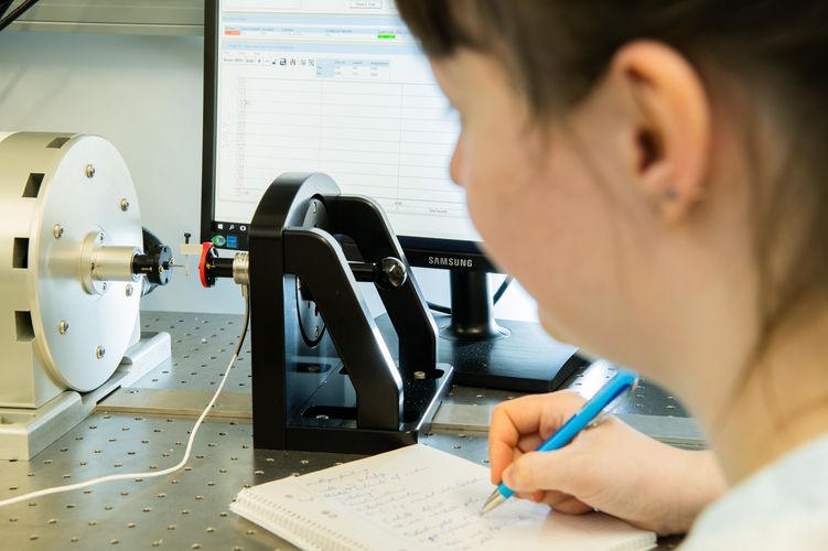 Forschung in der Bionik Eine Forscherin beobachtet einen Belastungsversuch mit einem Heuschreckenbein. Im Hintergrund steht ein Computerbildschirm.