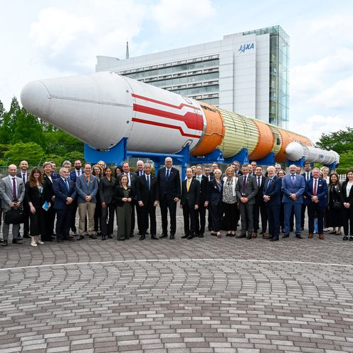 202605 Japanreise Gruppenbild mit Männern und Frauen. Im Hintergrund ist eine Rakete als Exponat zu sehen