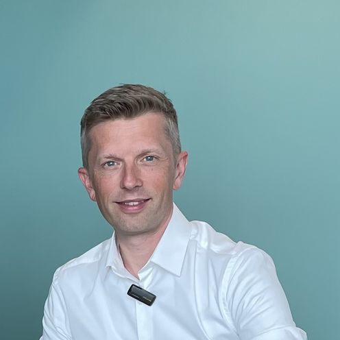 Dennis Kampen Sikora Dominik Uhr Zwei Männer sitzen am Tisch und alchen in die Kamera. Rechts von ihnen steht ein Laptop.