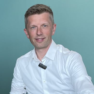 Dennis Kampen Sikora Dominik Uhr Zwei Männer sitzen am Tisch und alchen in die Kamera. Rechts von ihnen steht ein Laptop.