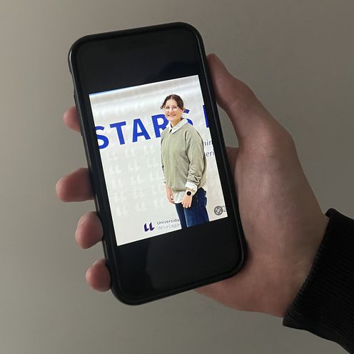 20260112_Foto neu Jule Sobanja Hand hält Handy. Darauf sieht man ein Foto einer jungen Frau vor einem Banner