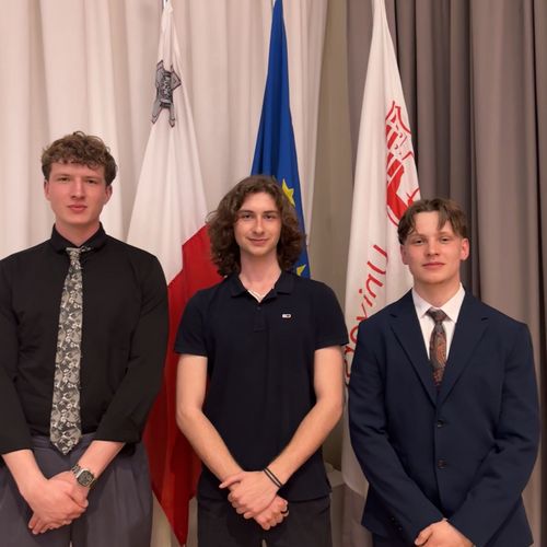 202605 STARS EU Student Board Konferenz Malta Gruppenbild mit drei jungen Männern. Sie stehen vor Fahnen.