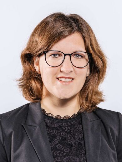 Auf dem Bild ist Kristina Lemmer zusehen. Sie hat schulterlanges graues Haar und trägt eine schwarze Brille sowie eine schwarze Bluse unter einem schwarzen Blazer. 