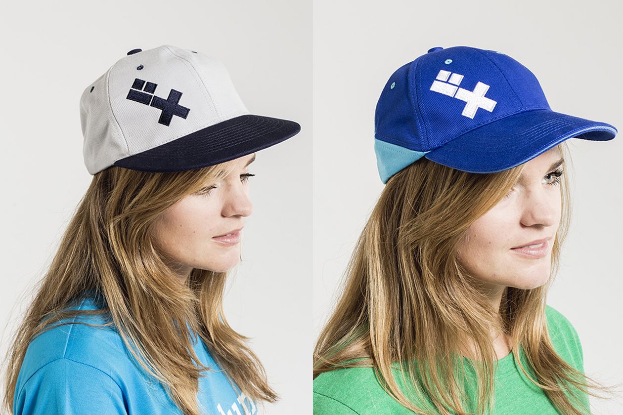 HSB Cap Ein Model trägt links eine grau-schwarze und rechts eine hell-/dunkel-blaue Cap mit HSB-Logo.