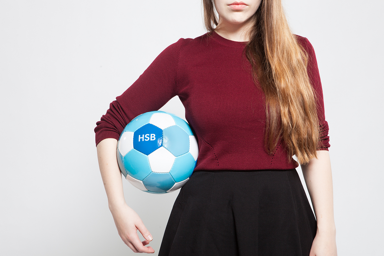 HSB Fußball Model hält einen blau-weißen Fußball mit HSB-Logo unterm Arm.