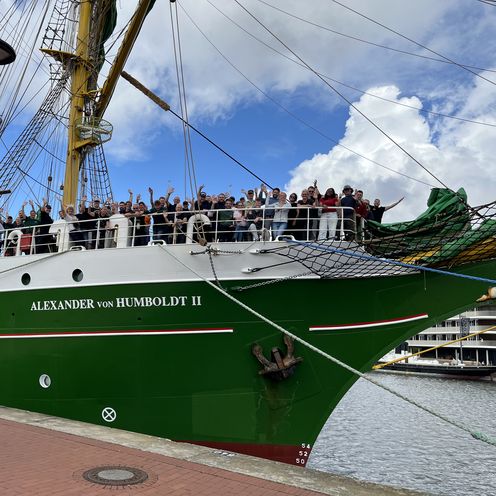 20260817 Alex-2 legt ab Segelschiff it grünem Rumpf. An Bord an der Spitze stehen Menschen und winken