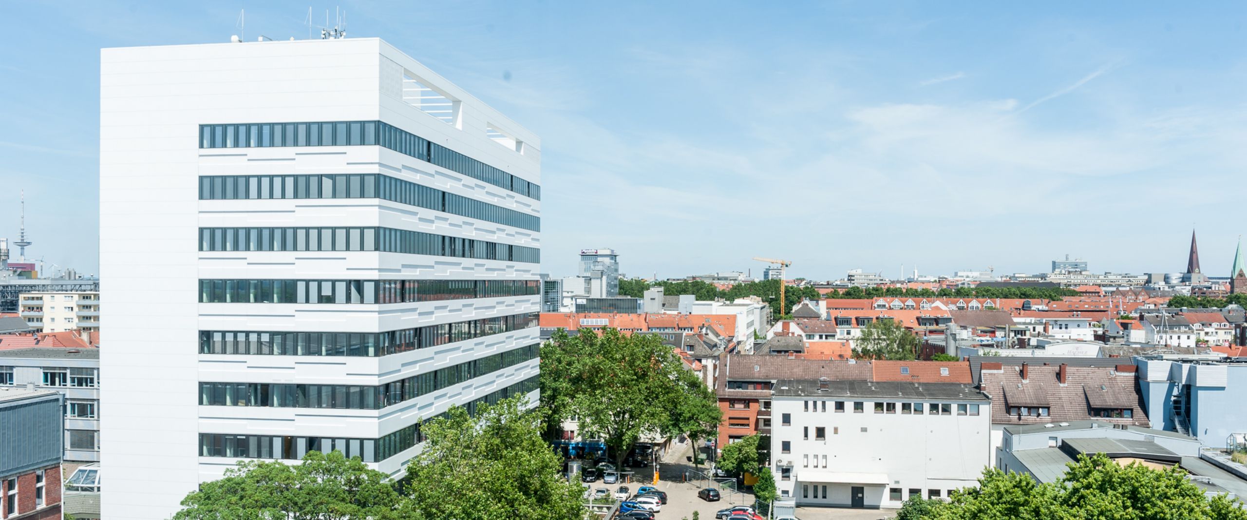 Luftaufnahme Campus Neustadtswall Auf dem Bild ist das AB-Gebäude des Campus Neustadtswall zusehen. Das Foto ist aus der Luft aufgenommen, sodass man außerdem noch blauen Himmel, grüne Bäume und einige Nebengebäude und den Parkplatz erkennen kann.