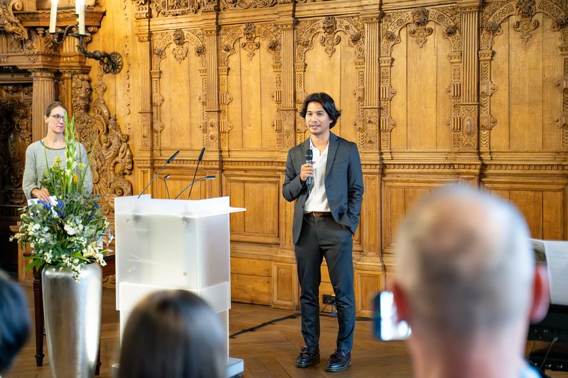 Junger Mann hält Rede in der oberen Rathaushalle vor großem Publikum. 