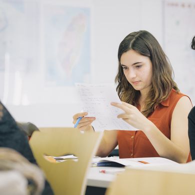 Studierende Zwei HSB Studierende sitzen an einem Tisch. Die linke HSB Studierende hält einen Zettel in den Händen und blickt konzentriert darauf. Der rechts neben ihr sitzende HSB Studierende blickt geradeaus nach vorn. Vor ihnen auf dem Tisch liegen Unterlagen.