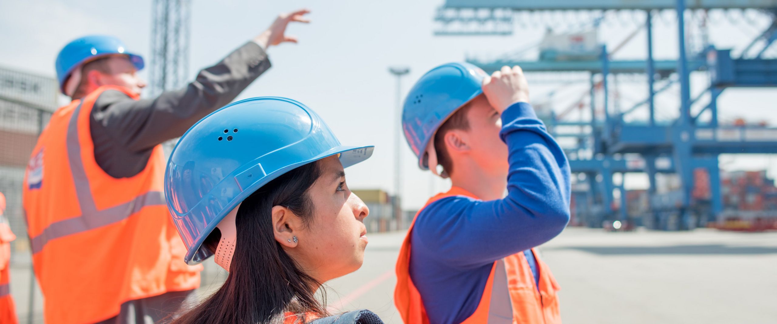Exkursion zum Containerterminal Ein Beschäftigter führt Studierende in Warnwesten und Schutzhelmen durch ein Containerterminal.