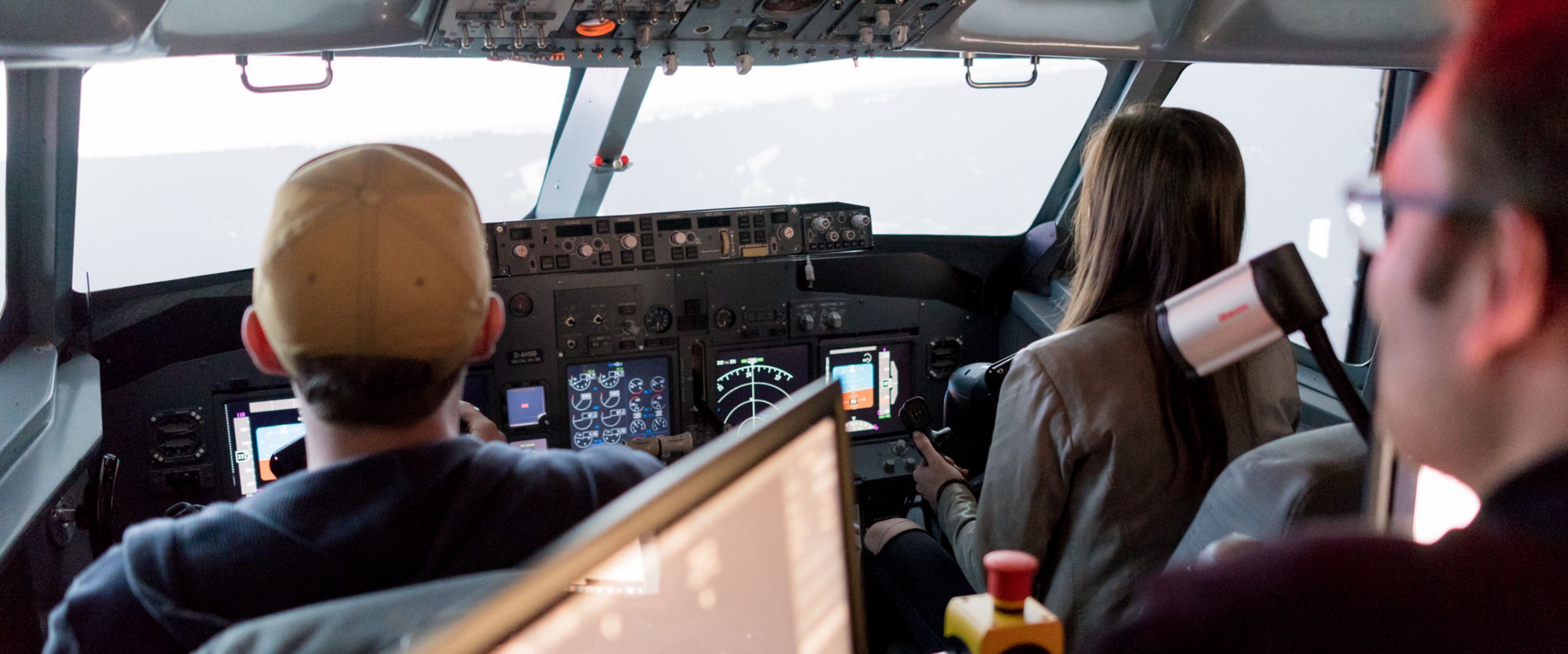 Flugsimulator Zwei Studierende und ein Professor sitzen im Cockpit eines Flugsimulators.