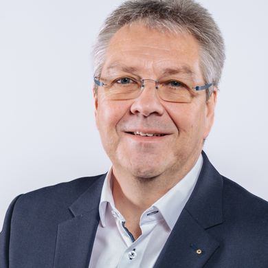 Helge Ellwart Auf dem Foto ist Helge Ellwart zu sehen. Er hat kurzes graues Haar und trägt ein weißes Hemd unter einer schwarzen Anzugsjacke.