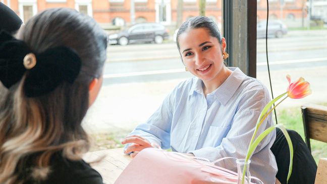 Studierende Junge Frau im Gespräch mit Studentin an einem Tisch