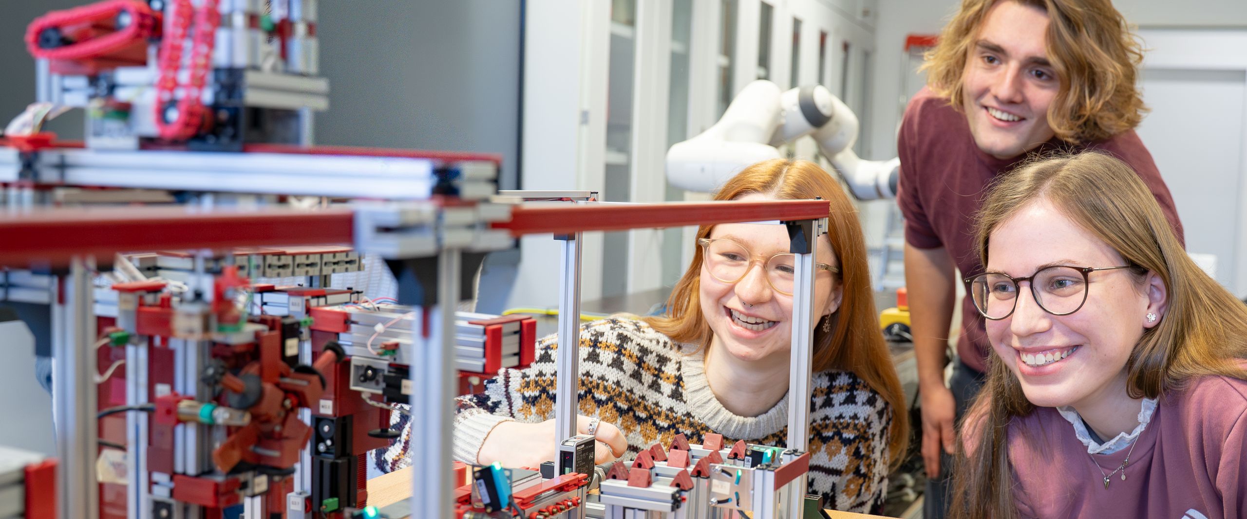 Modell automatisierte Förderanlage Auf dem Bild sind zwei Studentinnen und ein Student zusehen. Sie schauen sich ein Modell an.