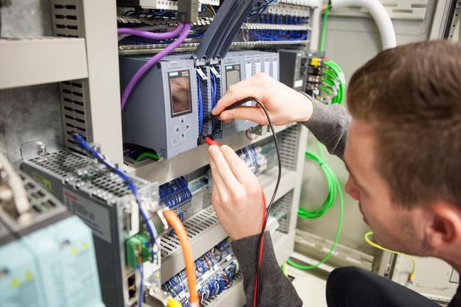Hands-on automation training Student working on an industrial control panel, testing connections with measuring probes.