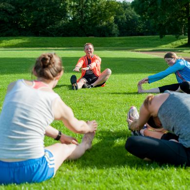RS4844__DSC653520170704.jpg Eine Personengruppe sitzt im Kreis auf der Wiese und dehnt sich.