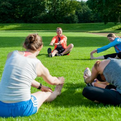 RS4844__DSC653520170704.jpg Eine Personengruppe sitzt im Kreis auf der Wiese und dehnt sich.