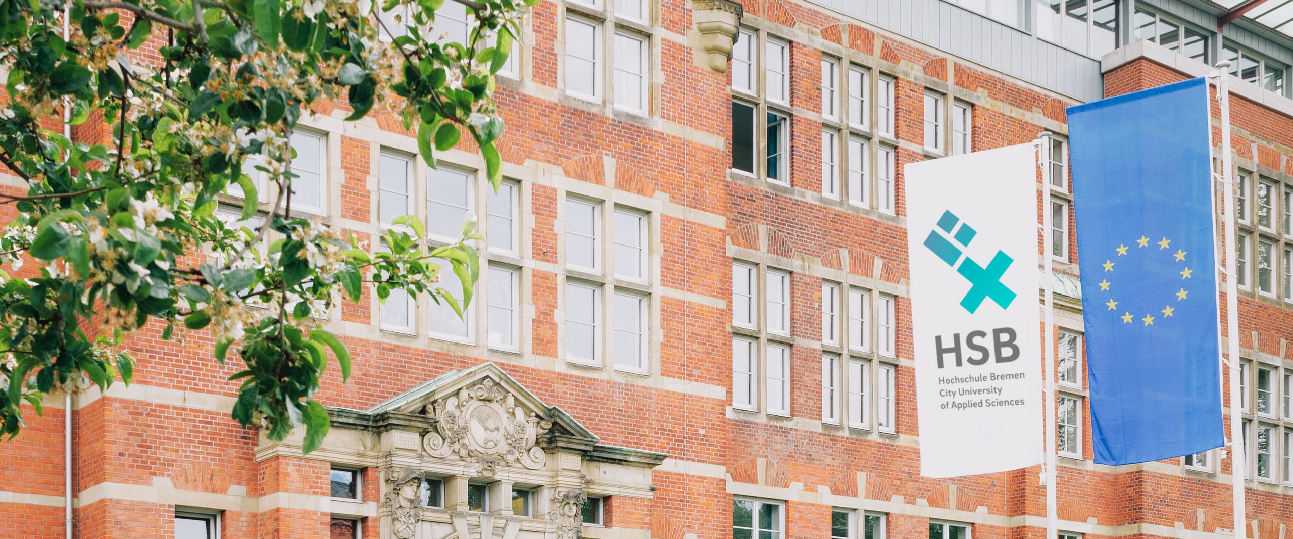 HSB-Gebäude M-Trankt plus EU Fahne Rotes Backsteingebäude an einer Wiese. Davor stehen Fahnen mit HSB-Logo und EU.
