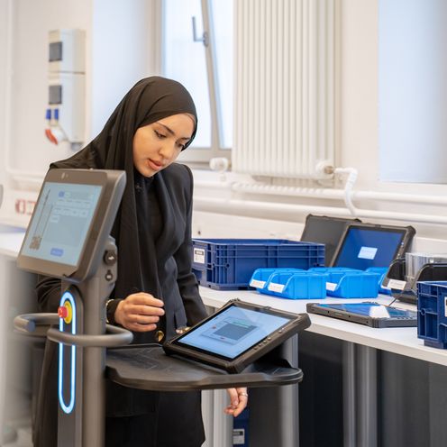 202605_Smart Factory Studentin Junge Frau mit Kopftuch steht am Tisch udn arbeitet an einem Tablet