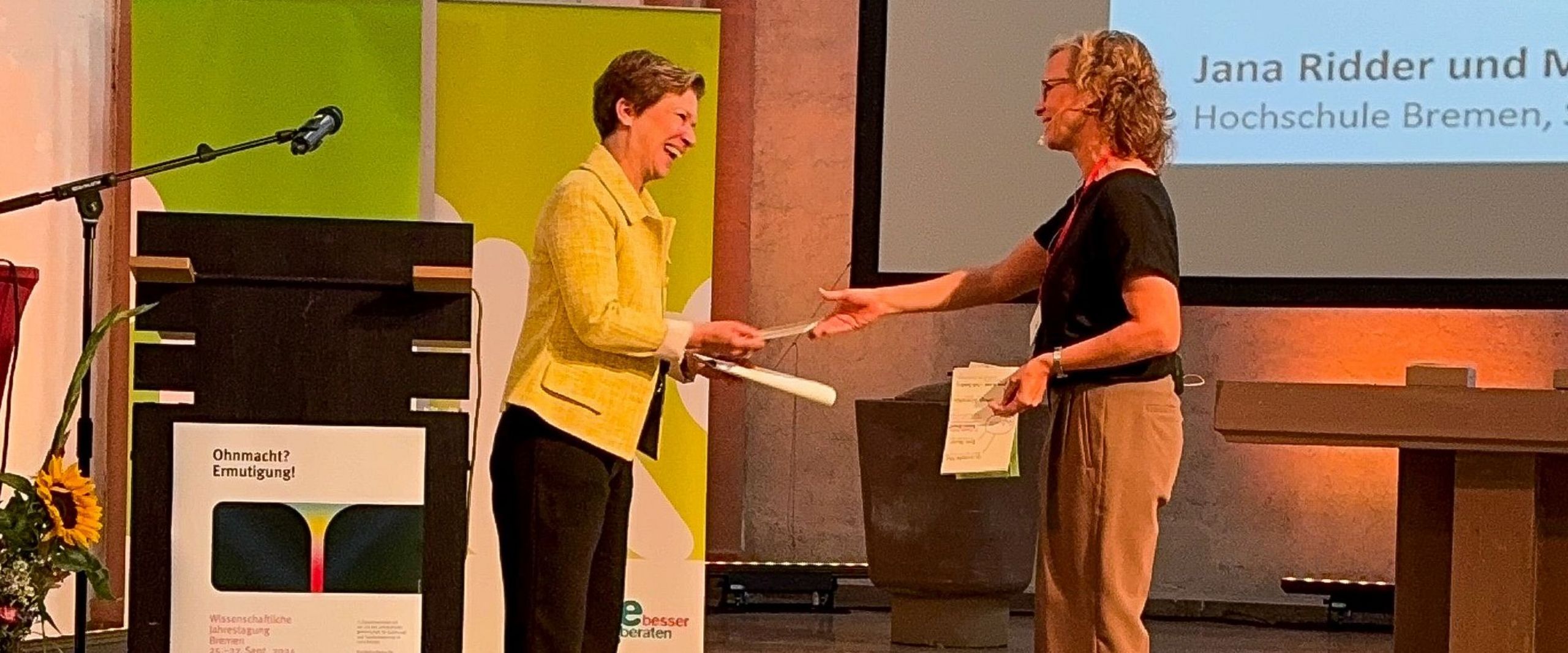 Zwei Frauen begrüßen sich an einem Podium