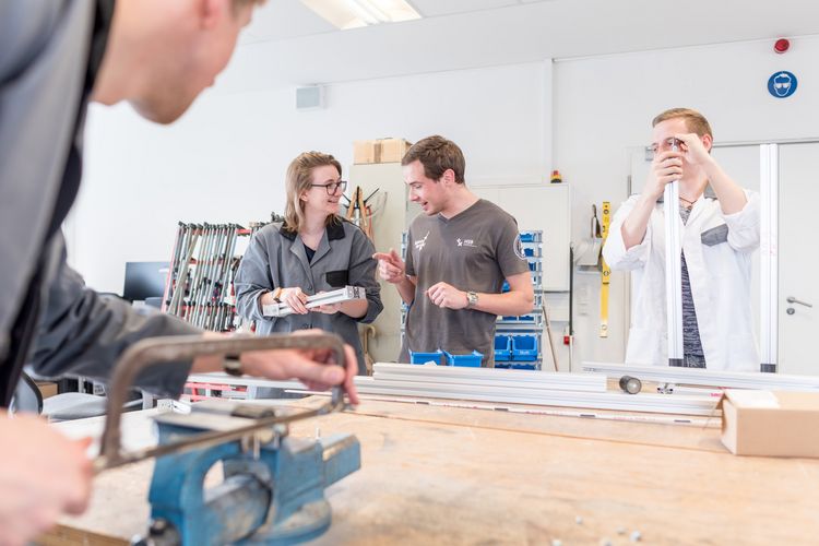 Werkstatt am ZIMT Eine Gruppe Studierende arbeitete an metallischen Bauteilen in einer Werkstatt.