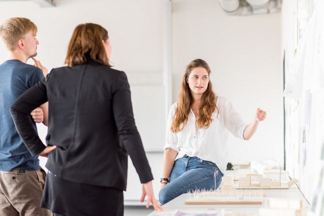 Eine Studentin präsentiert Prof. Andrea Dung und einem Kommilitonen ihre architektonischen Entwürfe. Eine Studentin präsentiert Prof. Andrea Dung und einem Kommilitonen ihre architektonischen Entwürfe.