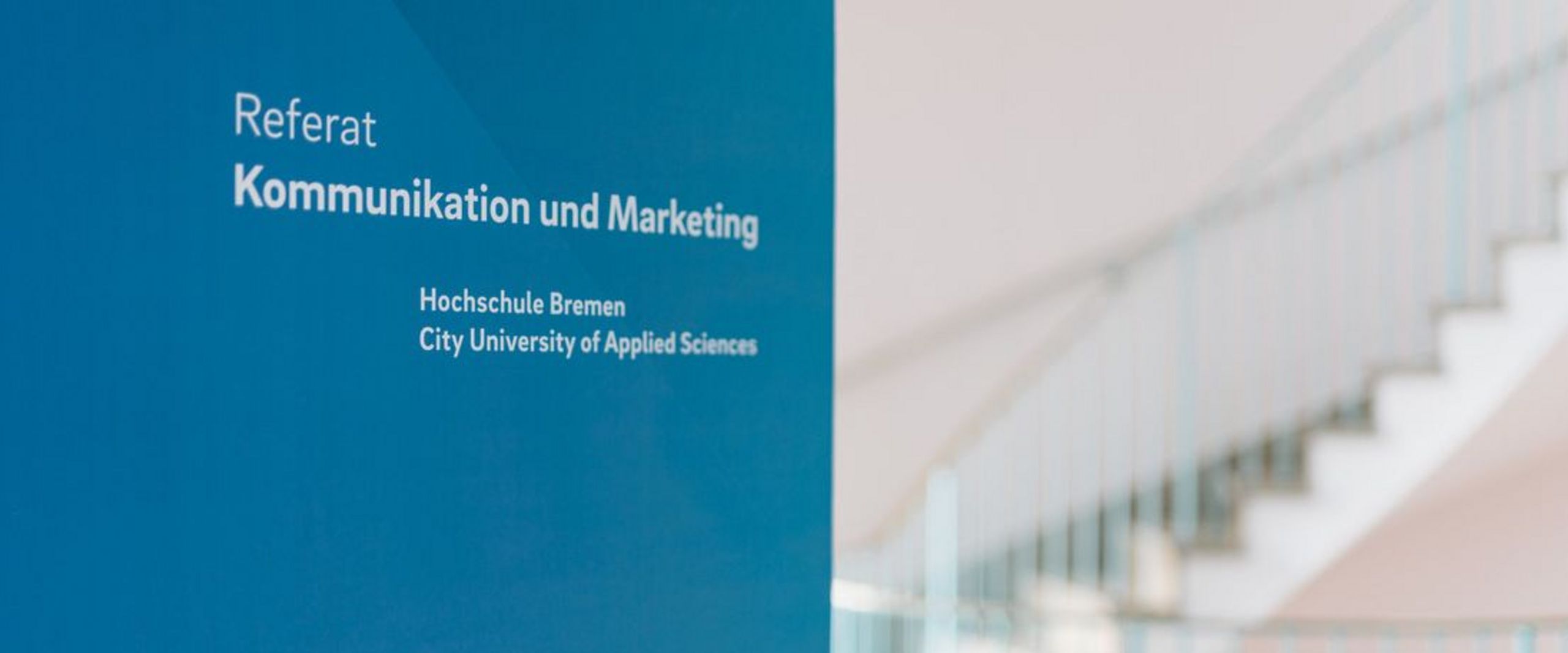 Schriftzug Referat Kommunikation und Marketing auf einer farbigen Wand im Design der Hochschule Bremen.