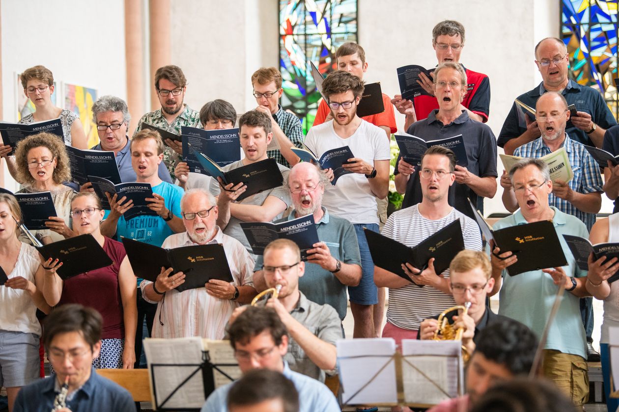 RS8548_20190629-0-218.jpg Frauen und Männer des Chors aufgereiht bei einem Auftritt mit Notenbüchern in den Händen.