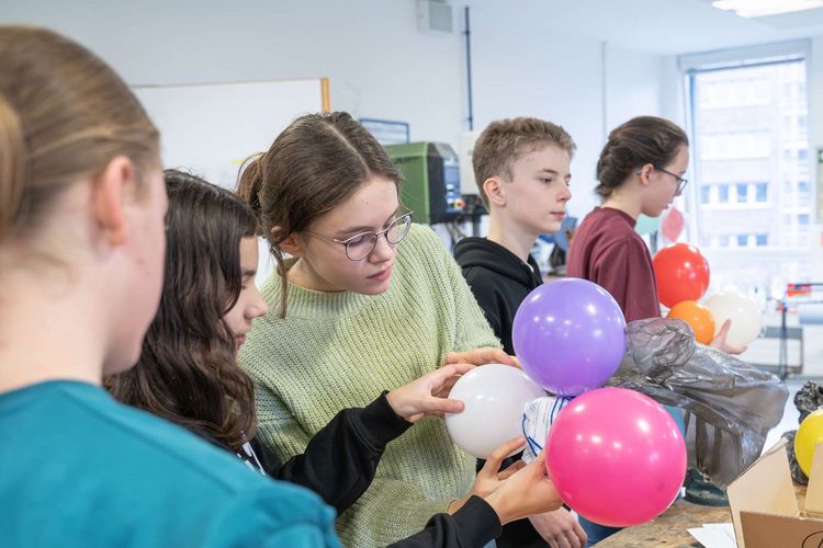 Konstruktionsbau Auf dem Bild ist eine Gruppe Schülerinnen zu sehen, die an einer Konstruktion aus rosafarbenden Luftballons bastelt.