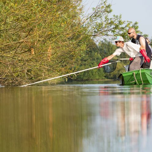 Foto PM Studie Baggersee Menschen im Boot auf einem See am Rande eines Ufers. Sie fischen im Wasser.